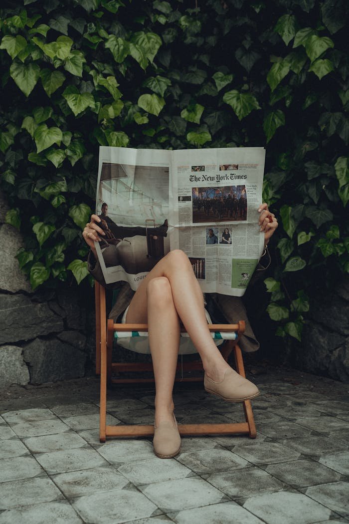 A young woman relaxing in a garden chair reading a newspaper, symbolizing leisure and relaxation.
